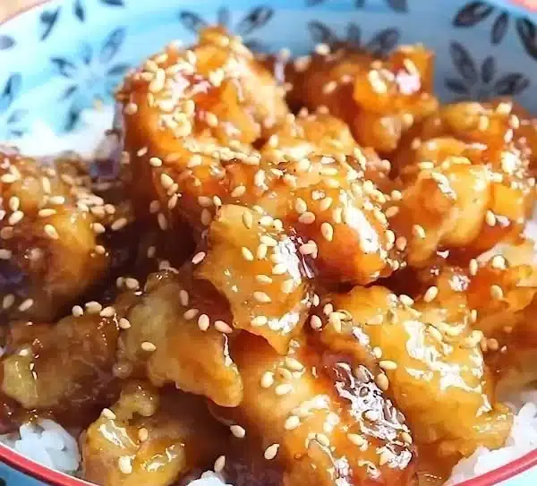 Delicious homemade Sesame Chicken garnished with sesame seeds and served with rice.